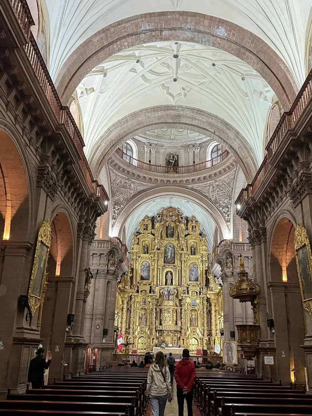Luxurious historic church interior with ornate gold altar, vaulted ceilings, and visitors admiring architecture.