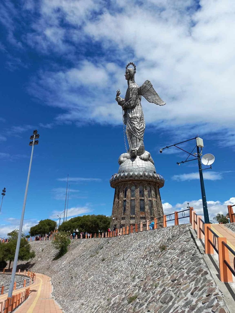 Majestic angel monument on a hill with blue sky and clouds, popular tourist attraction, significant cultural symbol.