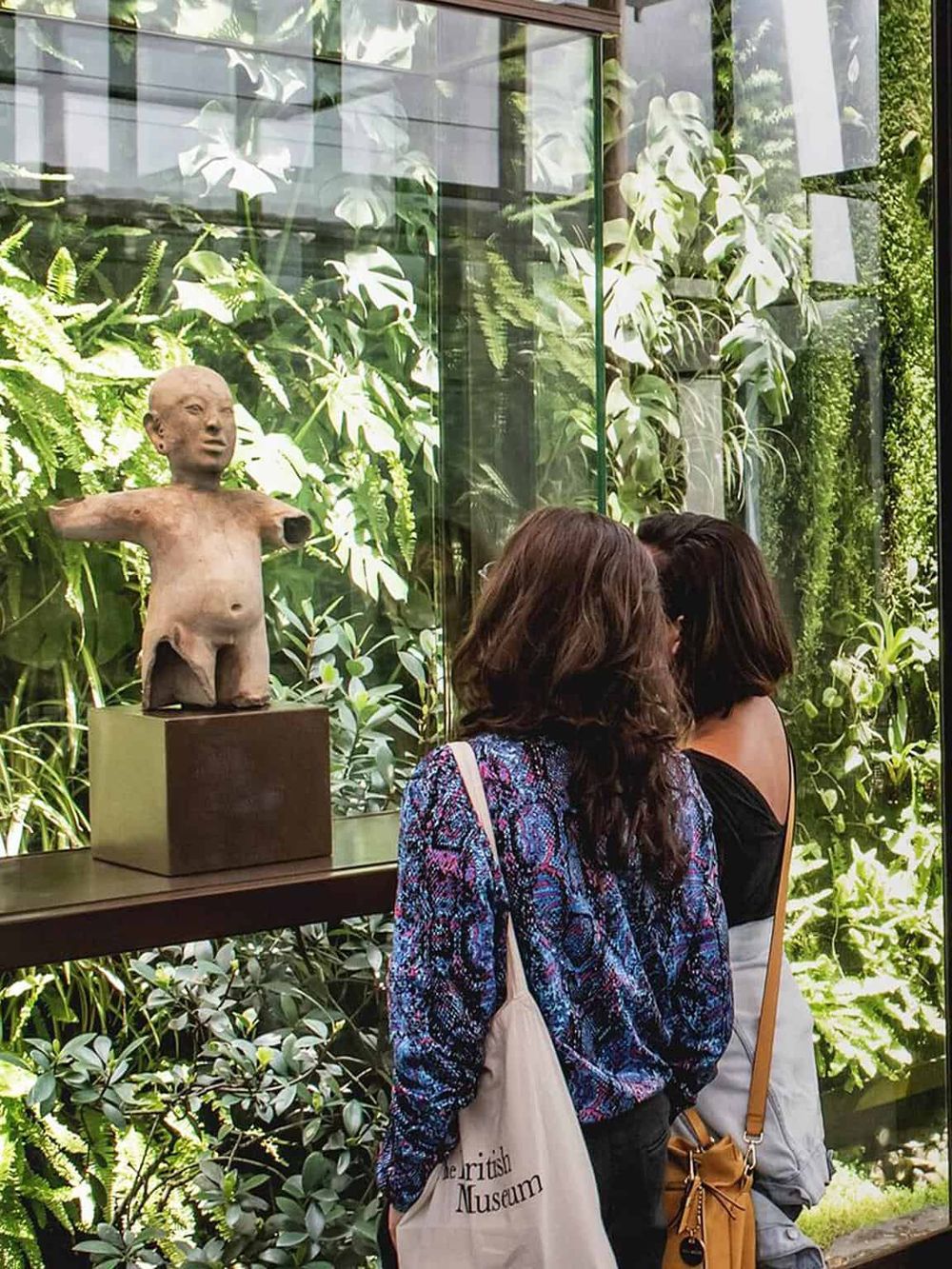 Ancient sculpture exhibit at Quest for Directions museum surrounded by lush greenery and visitors.