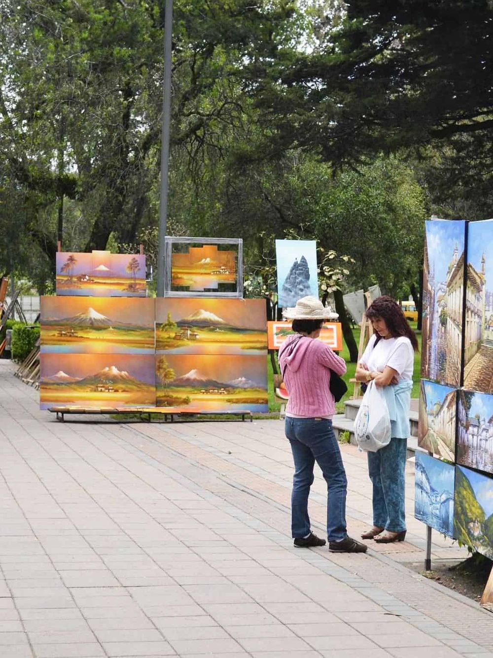 Colorful landscape paintings displayed outdoors at an art market or festival.