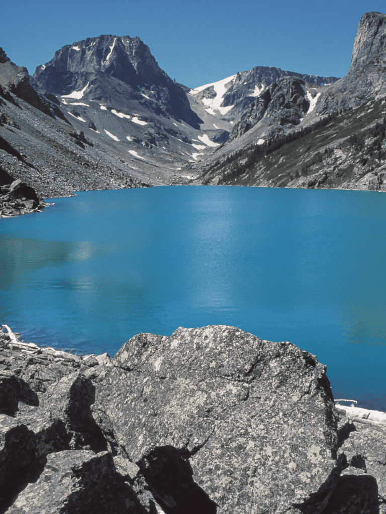 Stunning mountain lake surrounded by rugged peaks and snow patches, serene nature scenery for outdoor enthusiasts.