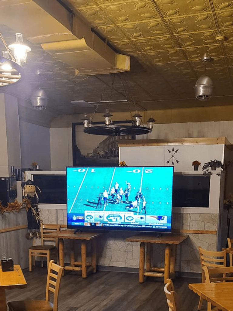 Cozy restaurant interior with TV sports display, wooden tables, and autumn decor, ideal for watching football games.