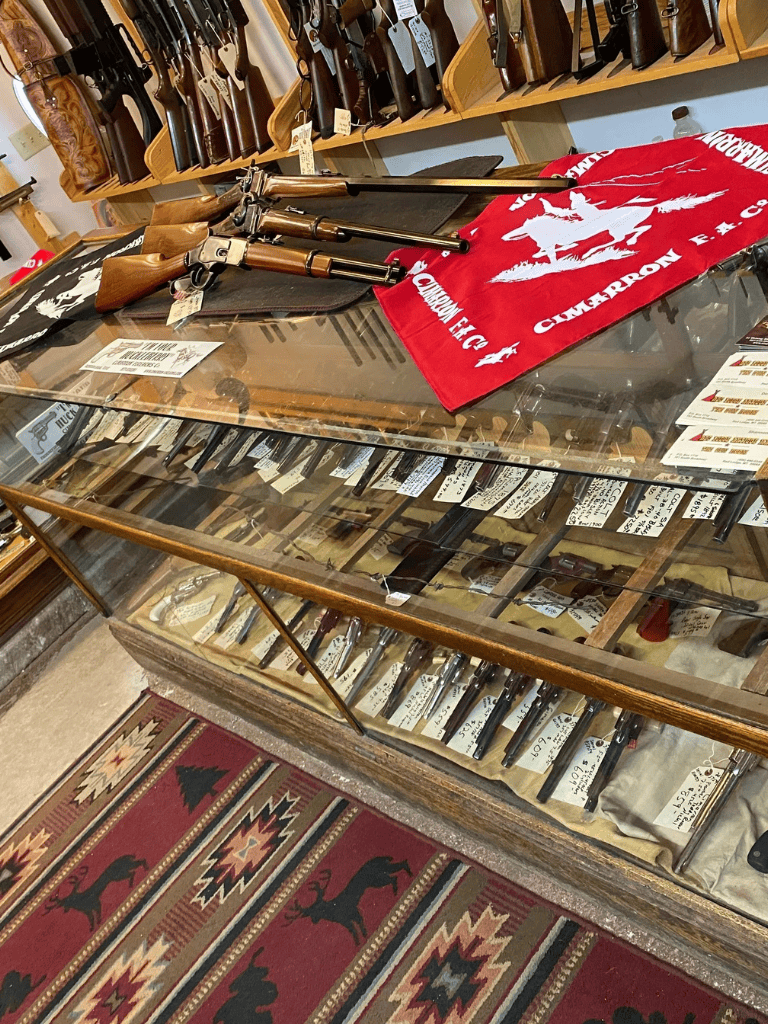 Cold War era rifles displayed in a firearm store with many pistols in the background.