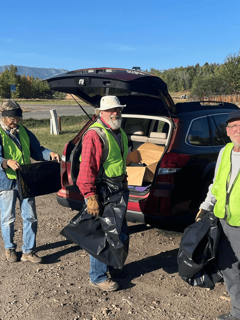 Volunteers preparing supplies for community service event, loading bags into car on sunny day with scenic background.