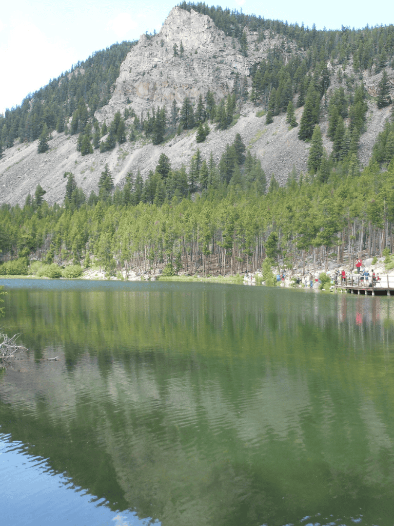 Calm mountain lake with forested shoreline and rocky mountain in background.
