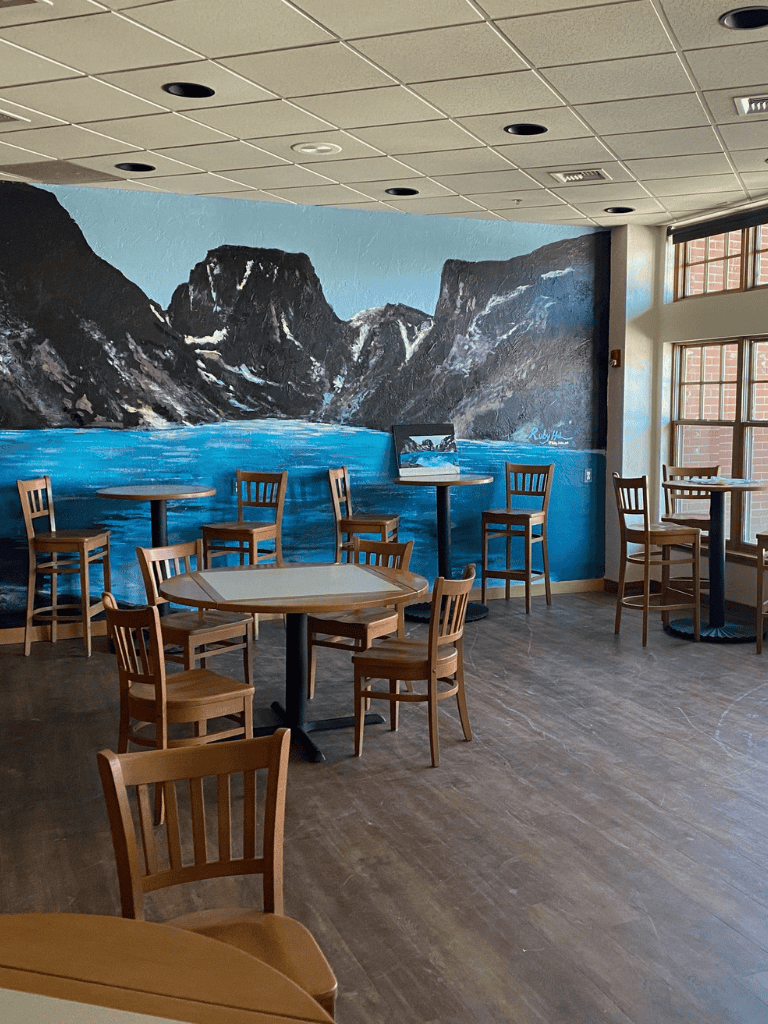 Quiet cafe interior with mountain mural and wooden tables, cozy atmosphere for relaxing or working.