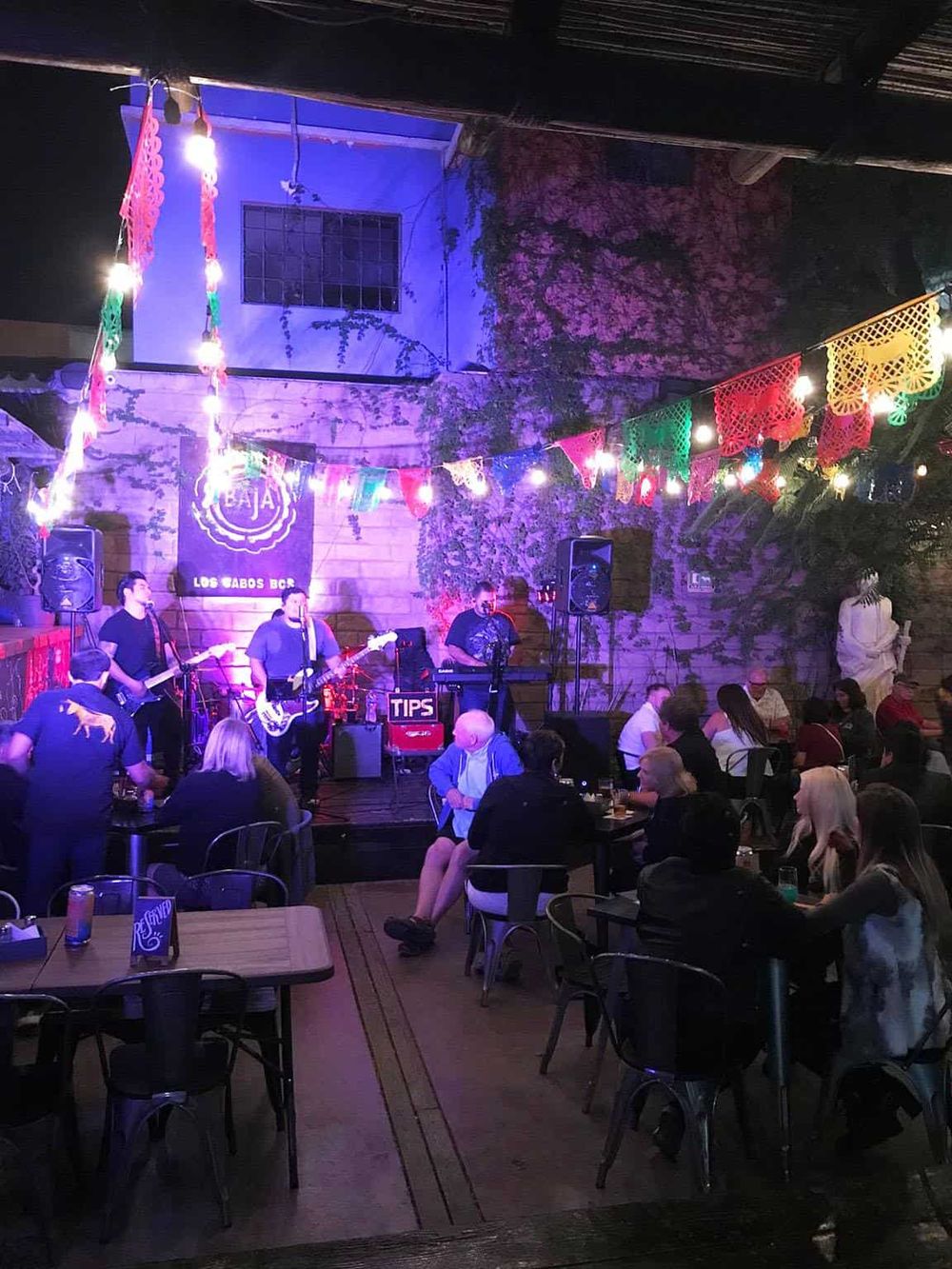 Live music performance at a vibrant outdoor bar with colorful decorations and an engaged crowd.