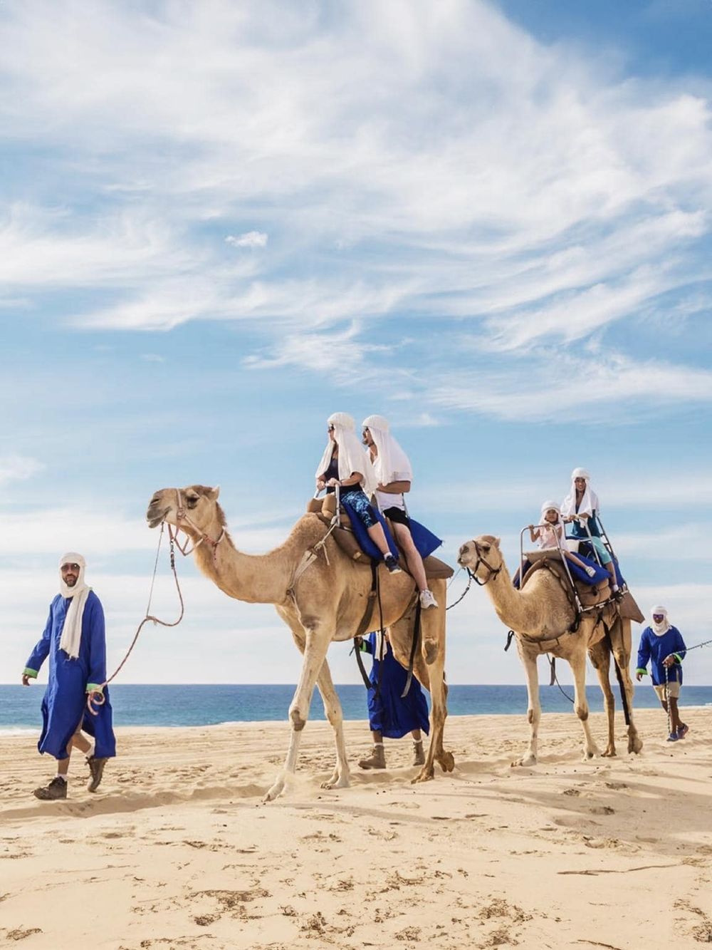 Camel riding adventure on the beach with guides, family, and scenic ocean backdrop, perfect for travel and tourism.