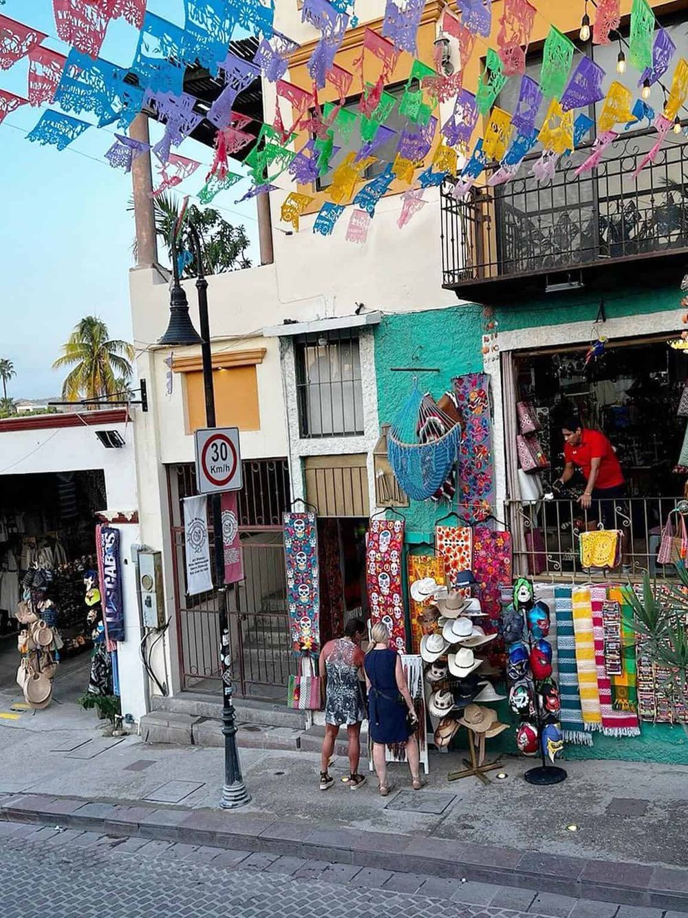 Colorful papel picado decorations hanging above a lively souvenir shop in a vibrant Mexican street scene.