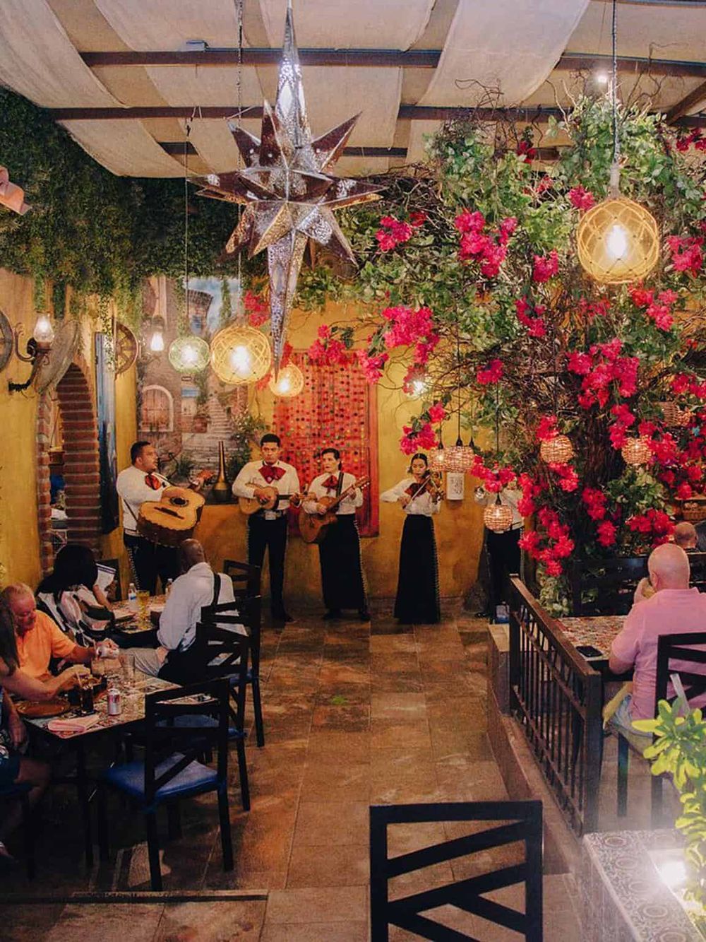 Live mariachi band performance in vibrant Mexican restaurant with colorful decor and floral accents.