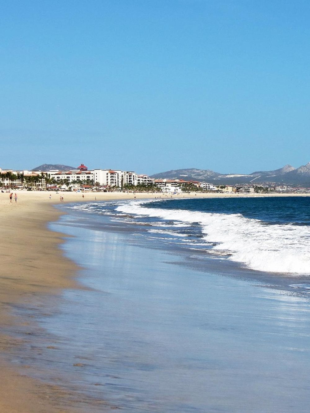 Serene beach with clear blue sky, white sands, and ocean waves, ideal for relaxation and seaside vacations.