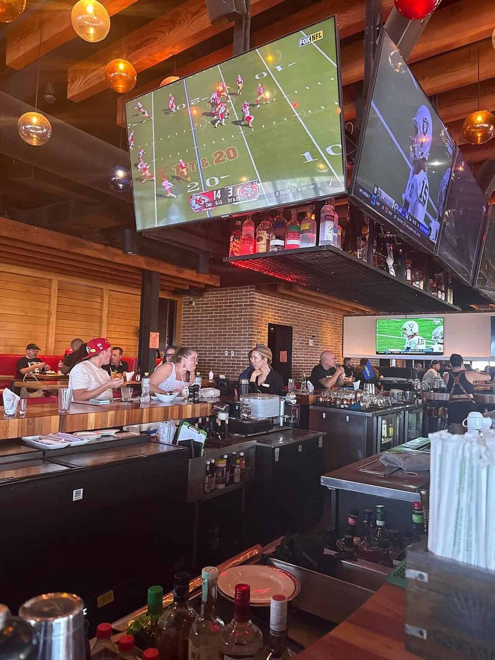 Bright sports bar with multiple screens showing football games and patrons enjoying snacks and drinks.