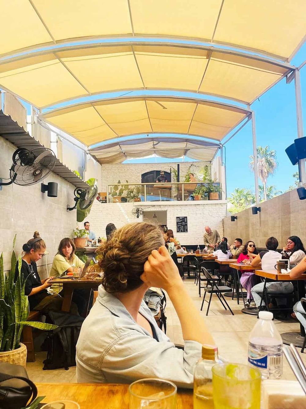 Bright indoor cafe with yellow shade canopy, featuring diverse people enjoying meals and drinks.