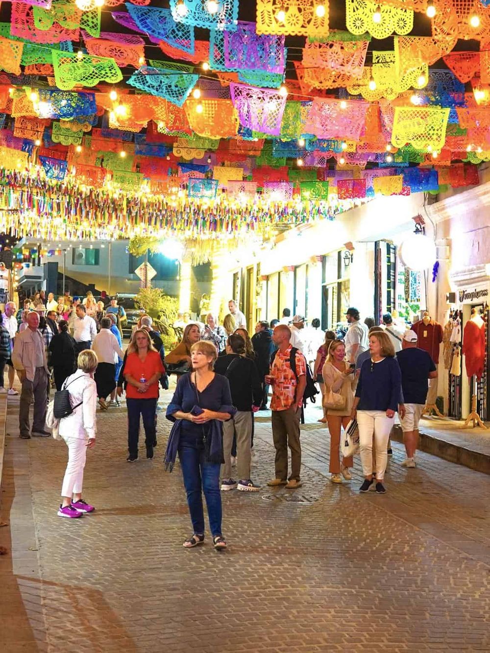 Colorful papel picado banners and festive lights at a lively outdoor Mexican marketplace festival.