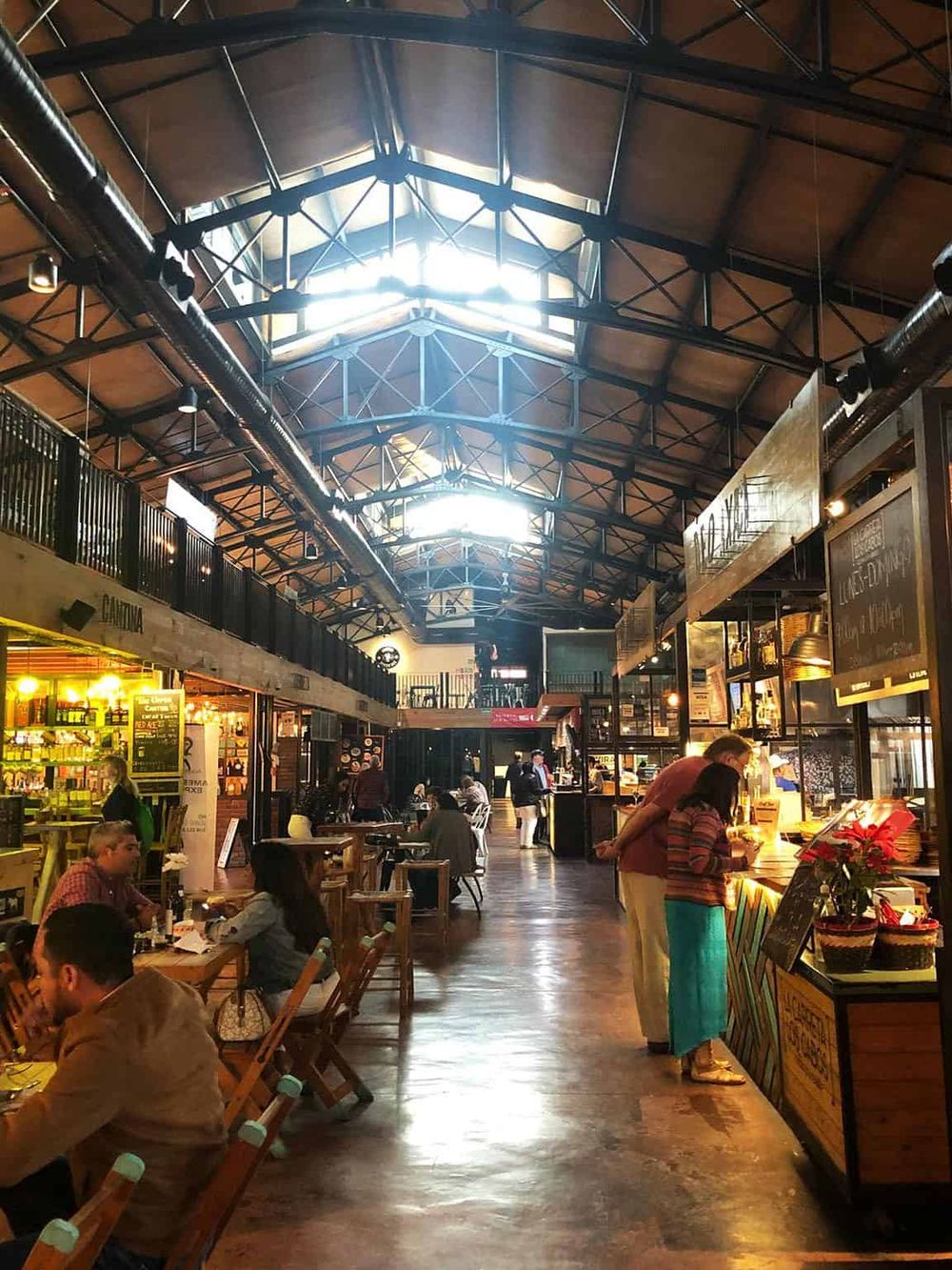 Bright indoor marketplace with diverse dining options and skylight ceilings, bustling with visitors enjoying fresh food.