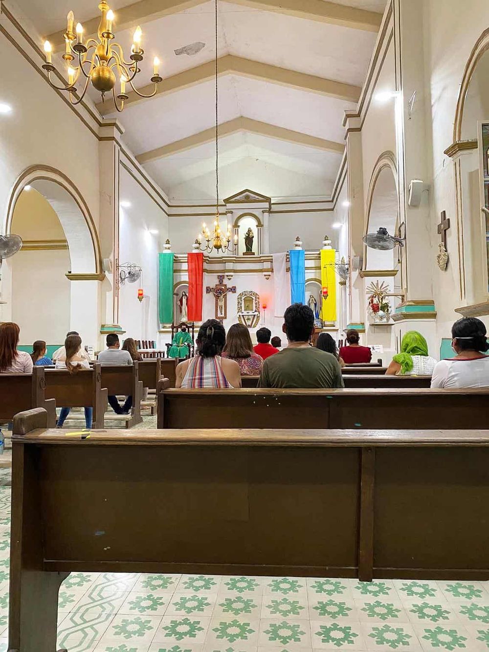 Colorful religious church interior with congregation attending service, altar with statues and flags, traditional decor.