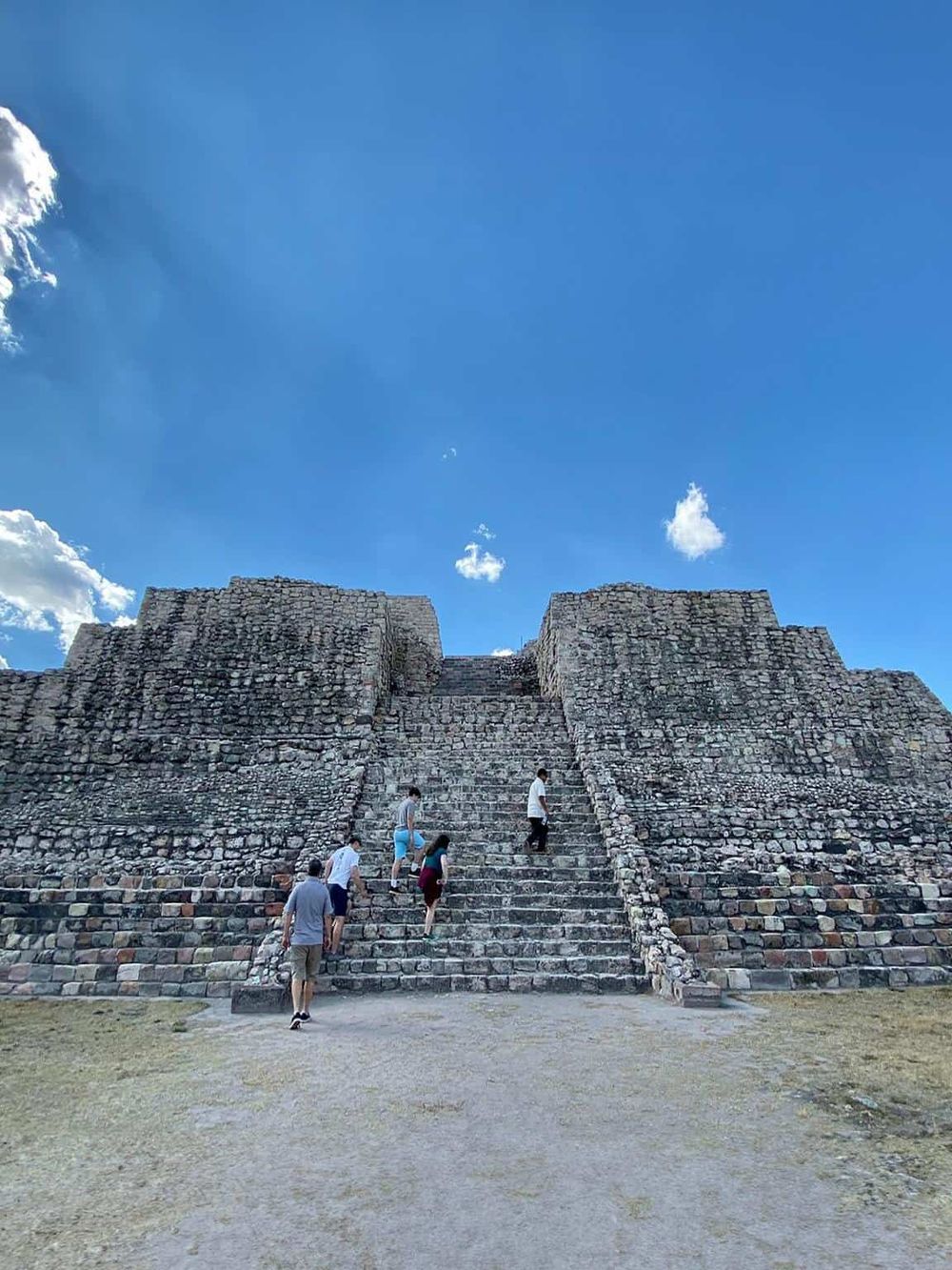 Ancient Mayan pyramid at Chichen Itza with tourists climbing the steps under a bright blue sky.