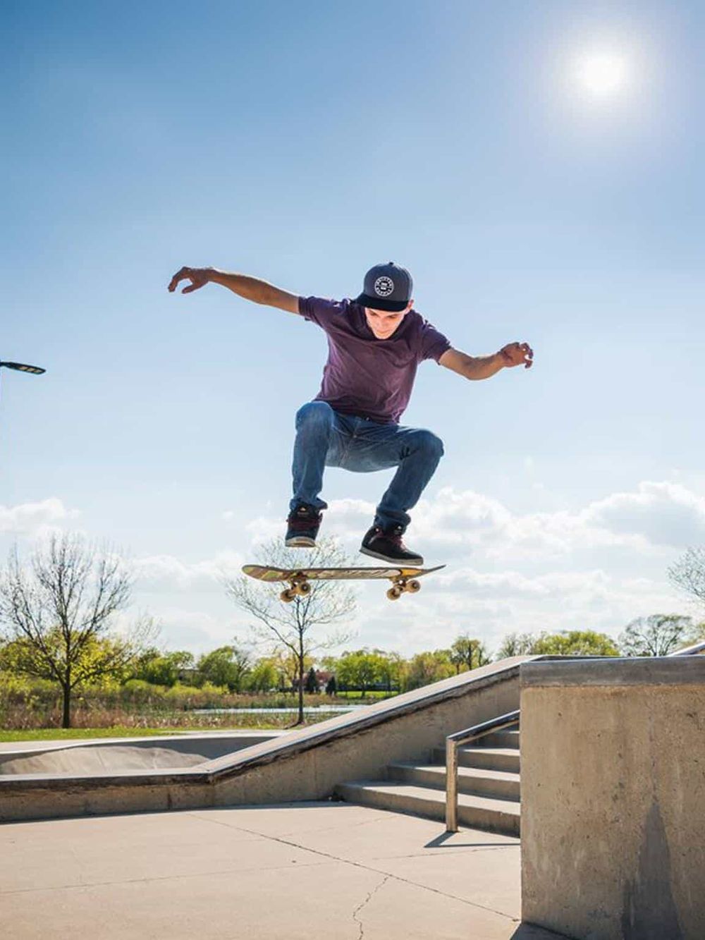 Skateboarder performing a trick at the skatepark on a sunny day with clear skies.