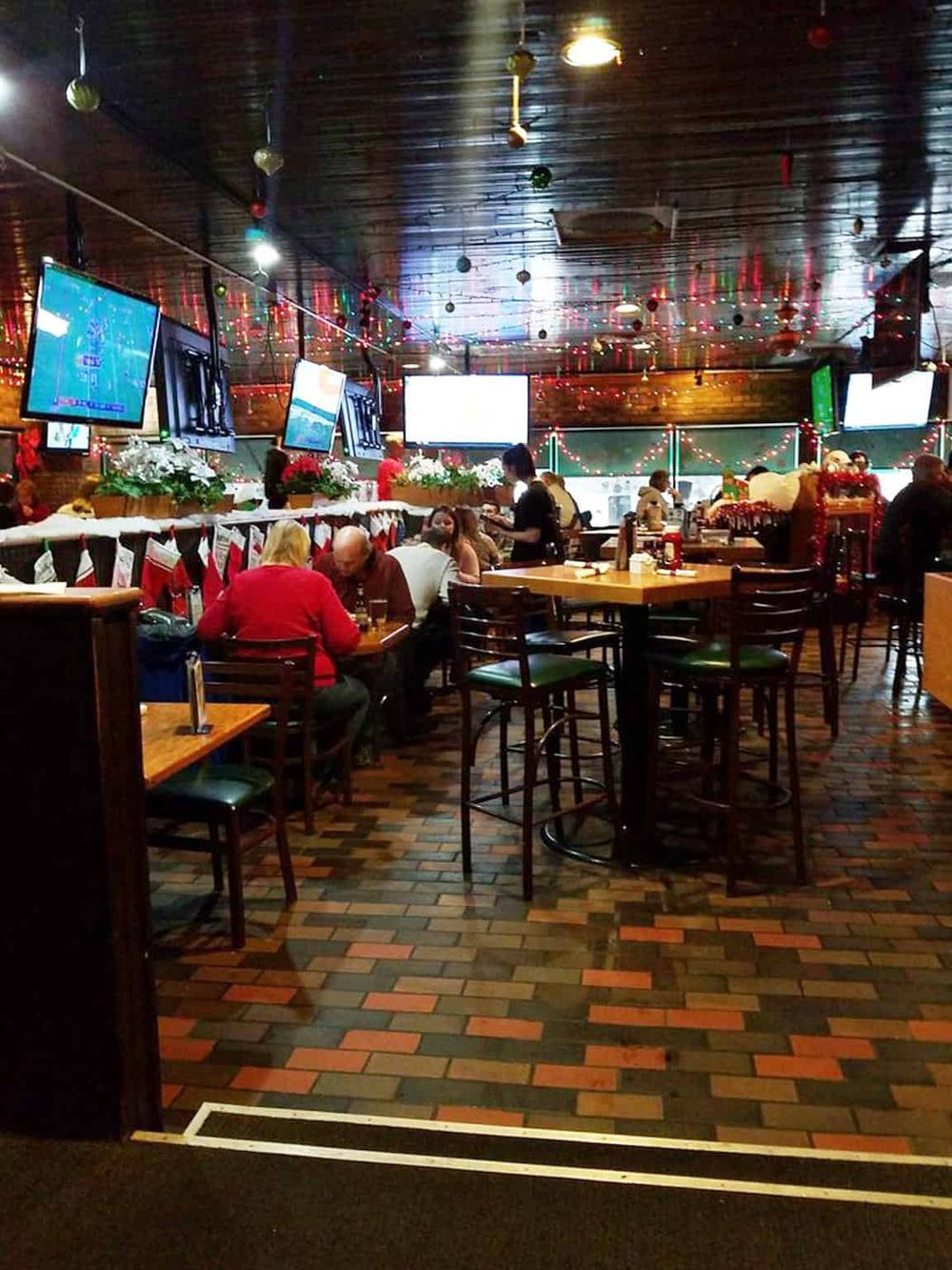 Cozy sports bar decorated for Christmas with multiple TV screens and festive lights, ideal for watching sports and holiday celebrations.