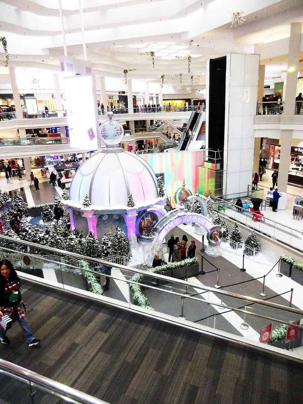 Bright indoor shopping mall with festive holiday decorations and Christmas trees.