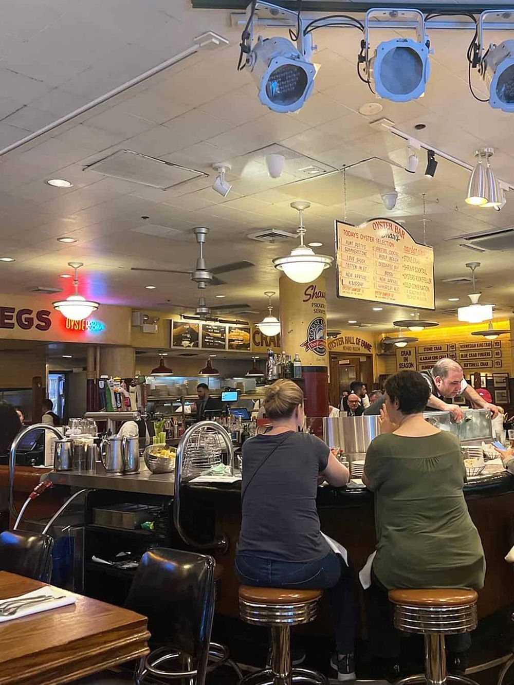 Busy oyster bar inside a seafood restaurant with patrons and illuminated menu board.