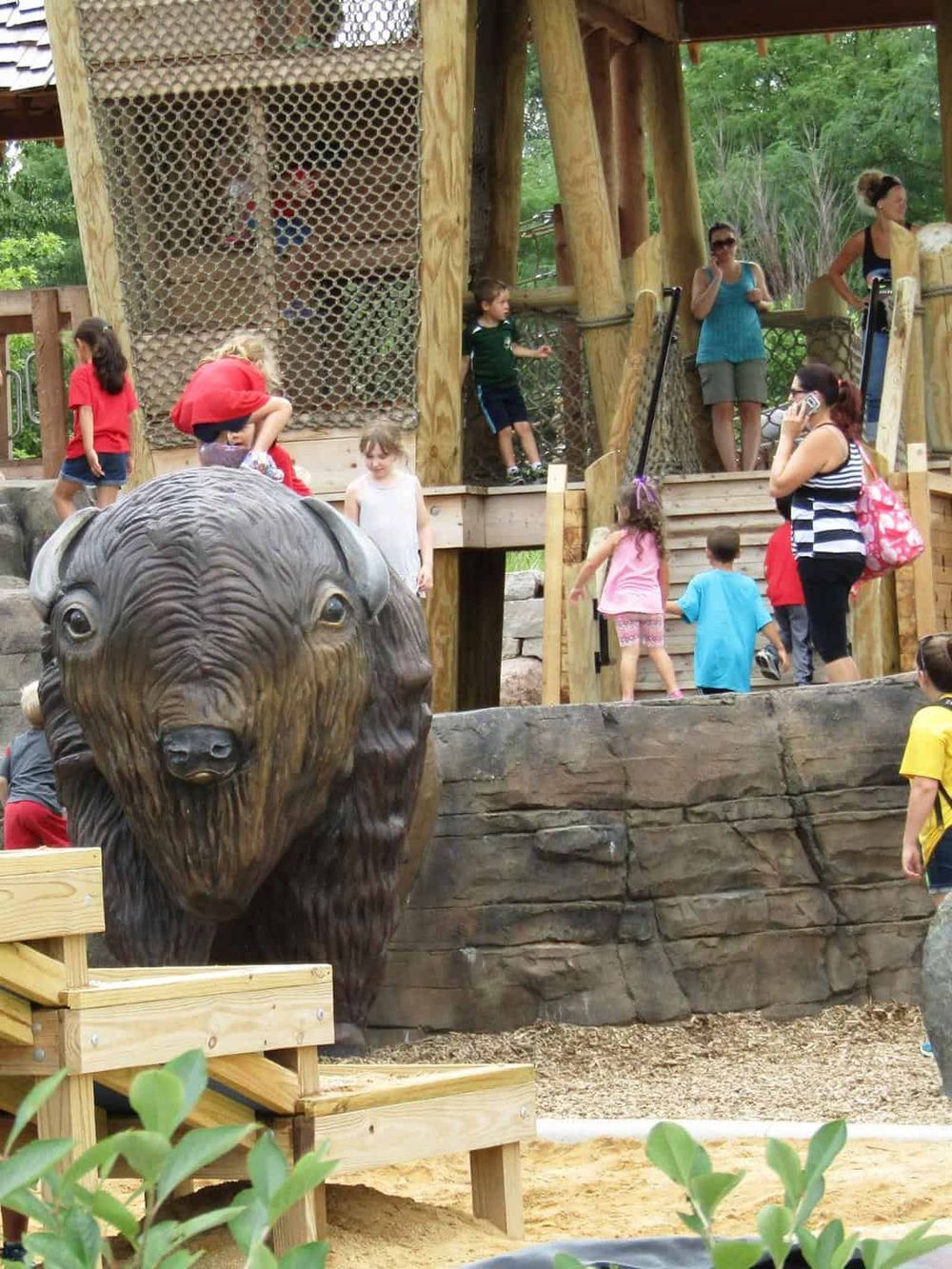 1. Kids playing on a wooden playground with a bear statue at QuestForDirections, a family-friendly outdoor park.