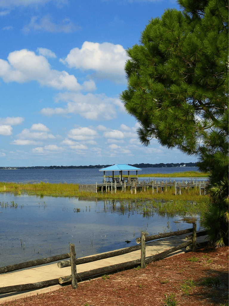 Tranquil lakeside scene with a wooden pier and gazebo under a bright blue sky.