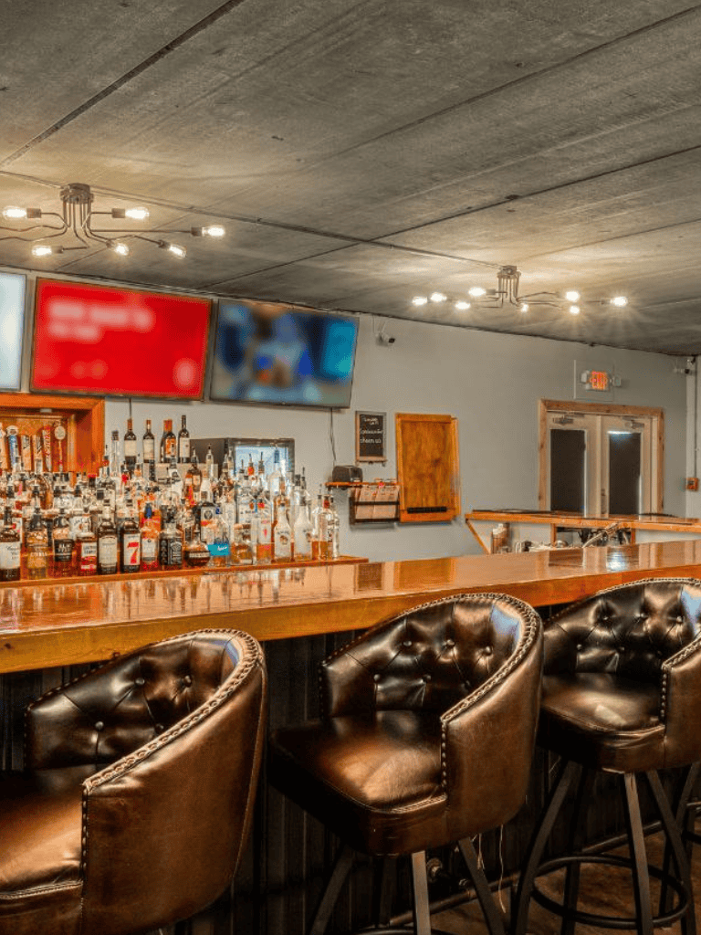 Upscale bar interior with liquor bottles, leather chairs, and multiple TV screens for a vibrant nightlife experience.