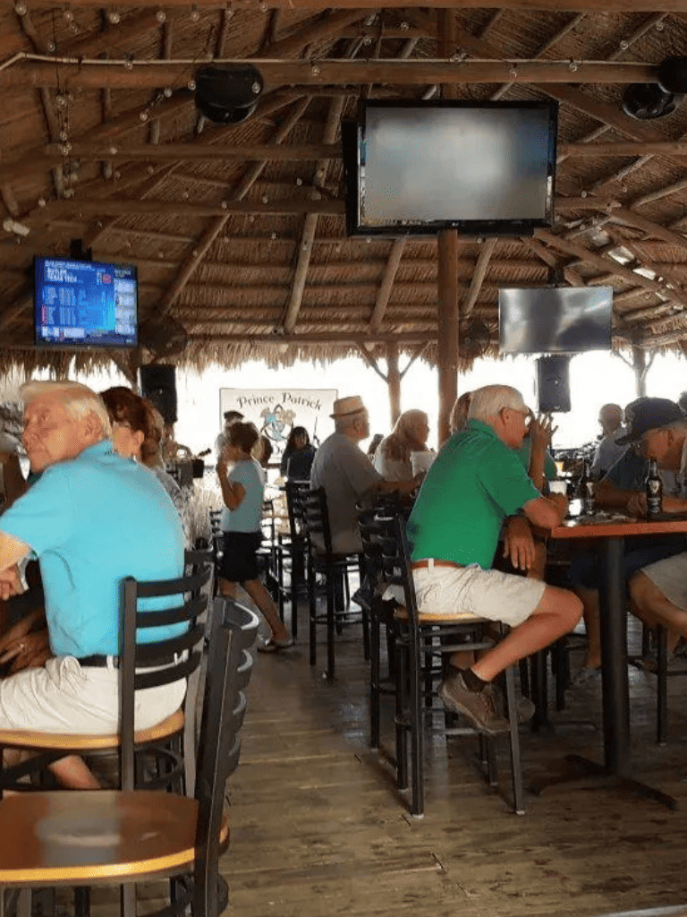 1. Casual group gathering at beachside restaurant with tiki hut roof and multiple TV screens.