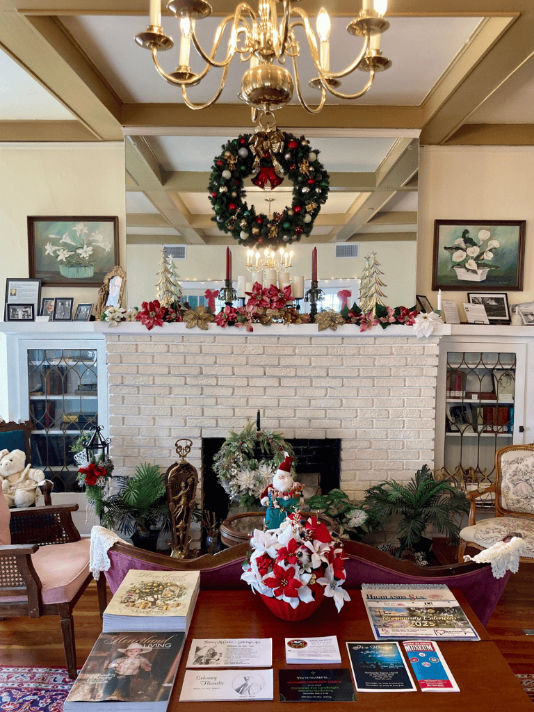 Christmas wreath hanging above decorated fireplace with holiday ornaments, candles, and greenery.