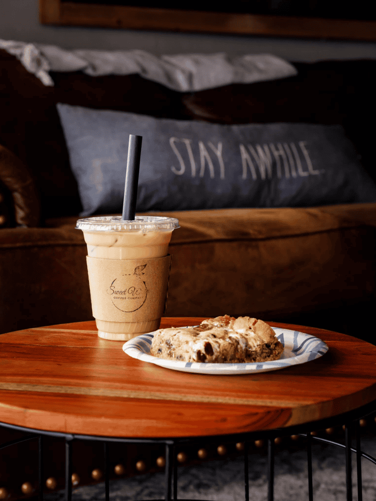 Creamy iced coffee with chocolate chip cookie on wooden table, cozy cafe setting.