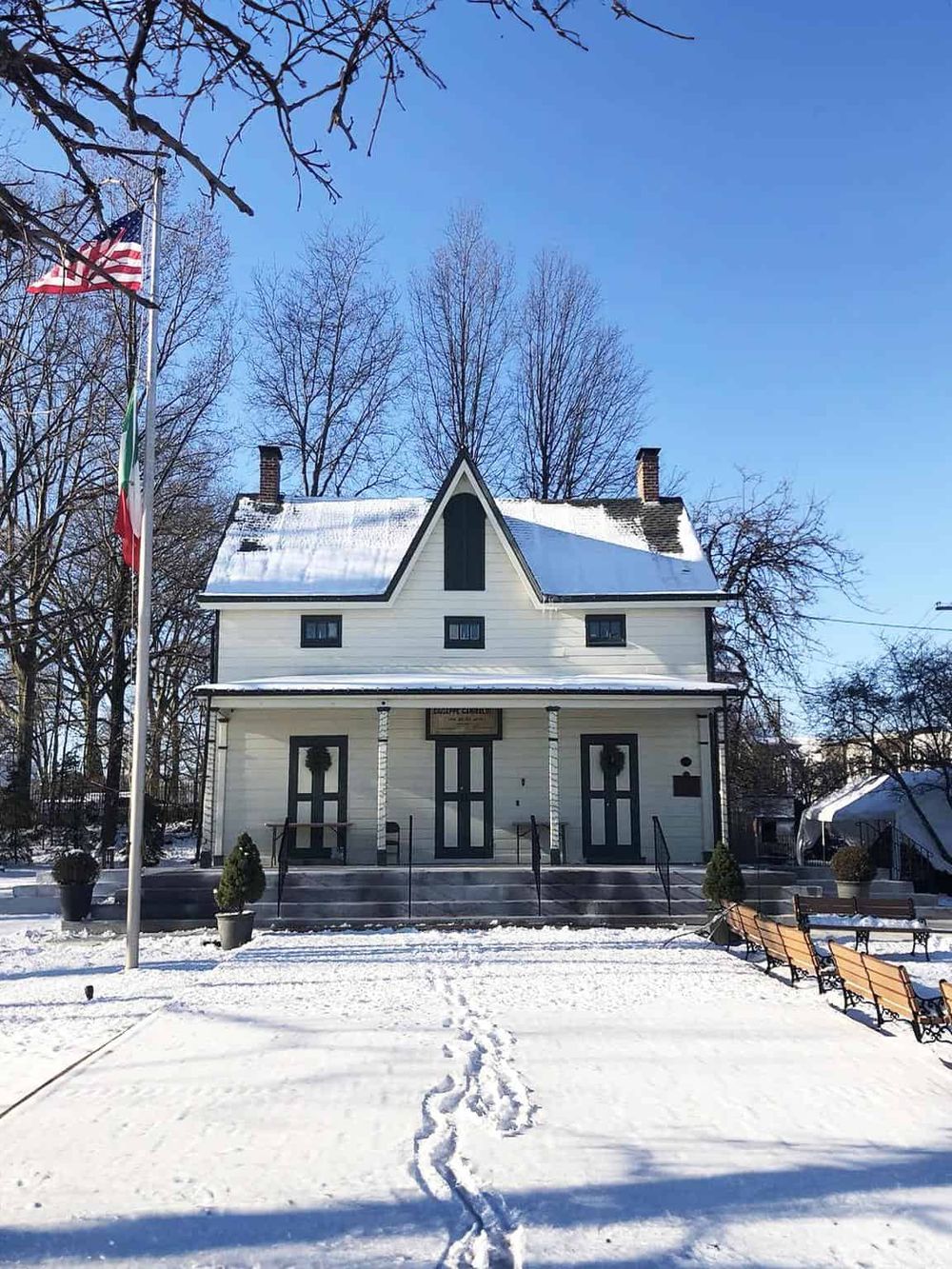 Historic snow-covered white house with flags, situated in a winter landscape, perfect for historic tours and photography.