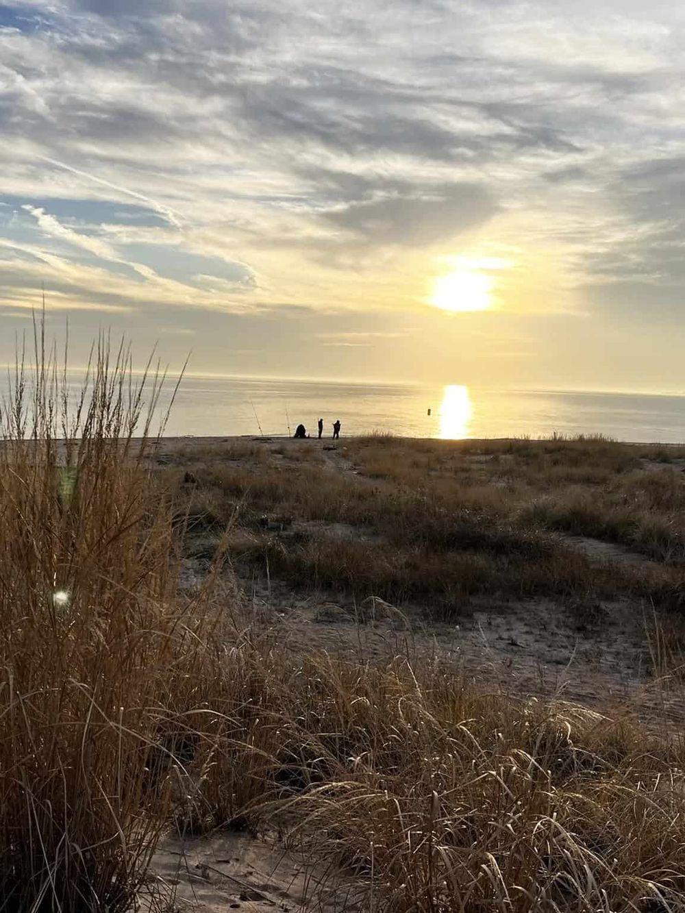 Serene beach sunset with people enjoying the view, golden sky, and calm ocean, ideal for relaxation and travel inspiration.