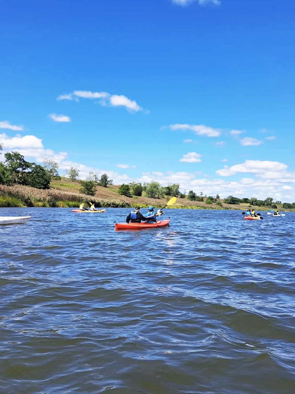 Kayaking on a scenic river with lush green hills under a clear blue sky. Perfect for outdoor adventure and nature exploration.