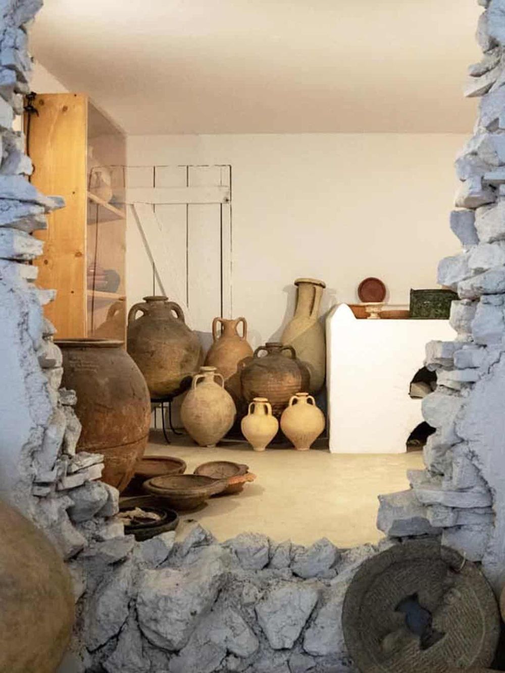 Traditional pottery collection displayed inside a rustic home with stone and white plaster walls.