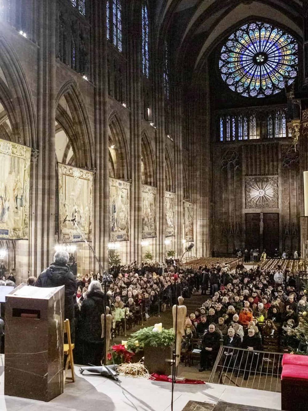 People attending a service inside a grand, gothic-style cathedral with stained glass windows.