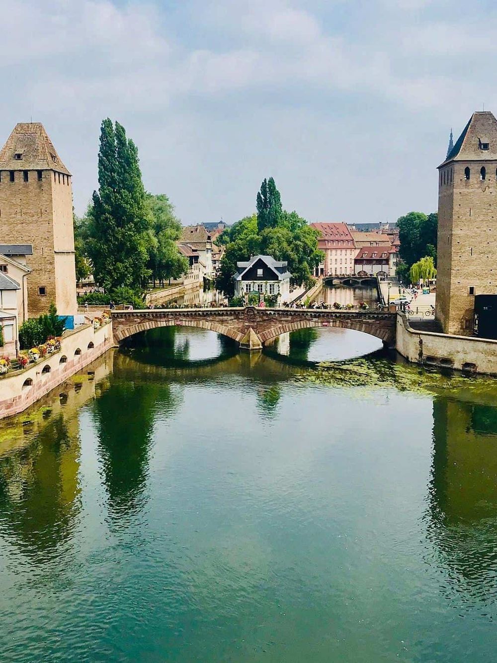 Medieval European city river with stone bridges, historic towers, and lush greenery, showcasing top travel destinations.