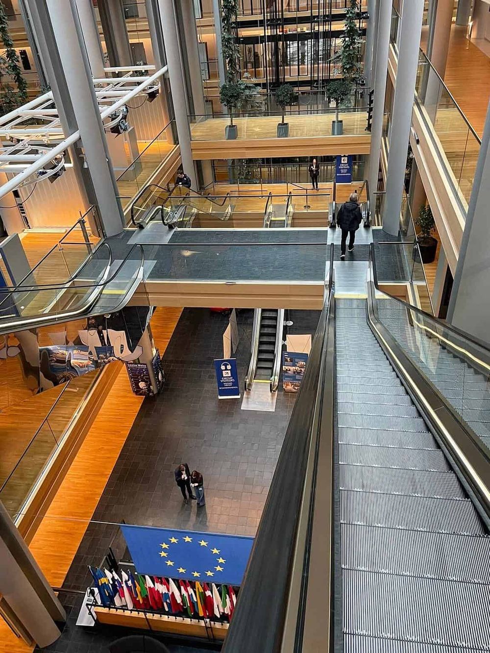 Bright modern office building interior with escalators and EU flags, showcasing professional workspace atmosphere.