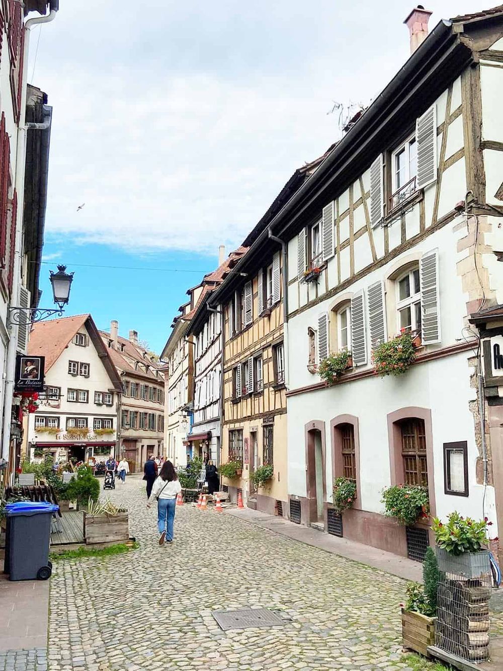 Charming European cobblestone street with historic half-timbered buildings and outdoor cafes.