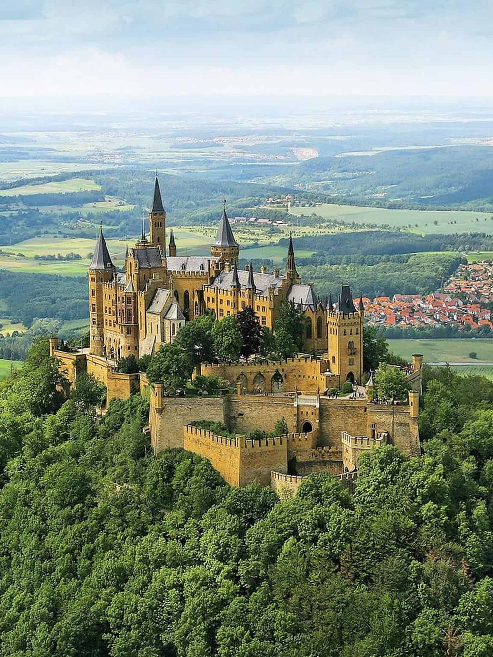 Fairytale castle atop lush green hill with scenic landscape, perfect for travel and tourism inspiration.