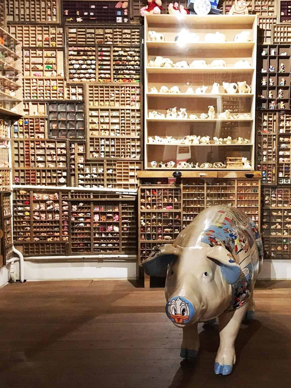Colorful miniature toy figures display wall with duck cartoon pig sculpture at QuestForDirections store.