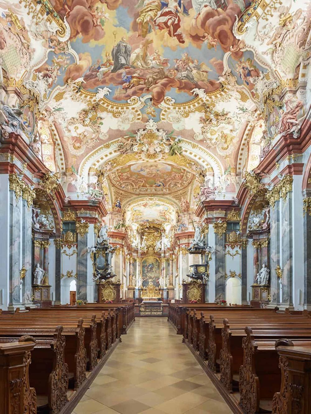 Baroque church interior with ornate gold details and colorful ceiling frescoes.