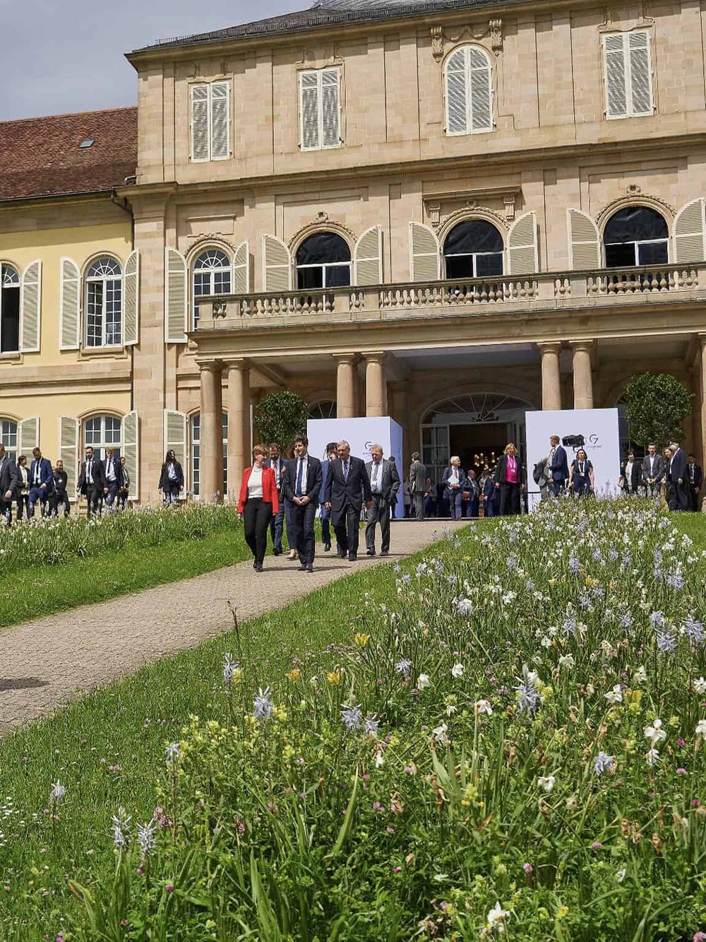 Elegant mansion with group of business professionals at event entrance, outdoor setting, lush garden, corporate gathering, QuestForDirections.