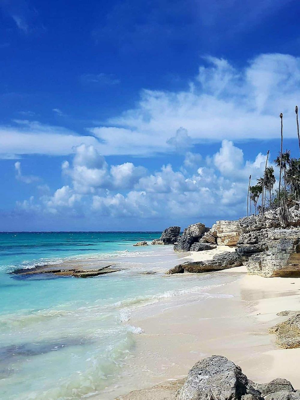 Stunning tropical beach with turquoise waters and rocky shoreline under a bright blue sky.