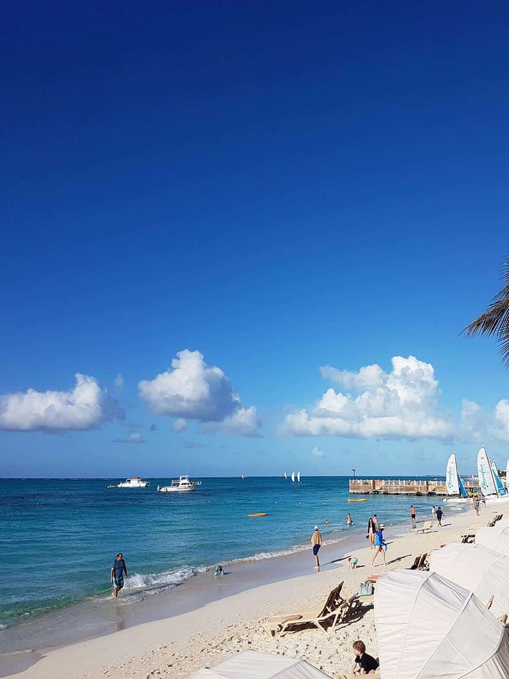 Pristine beach with blue skies, sailing boats, and relaxing lounge chairs, ideal for vacation and coastal adventures.