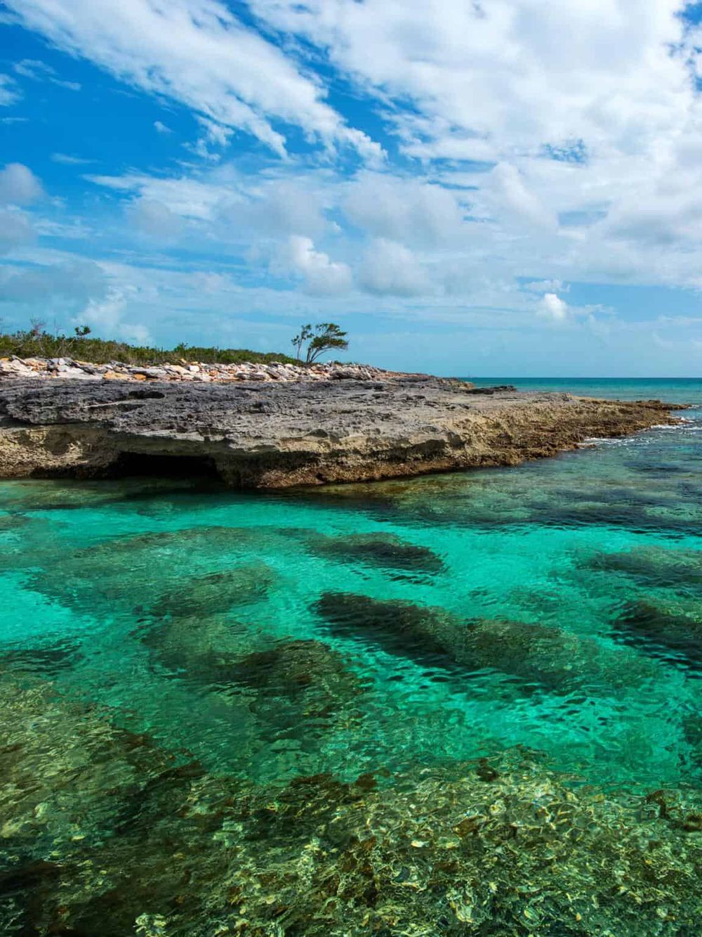 Vibrant turquoise ocean water with rugged rocky shoreline and a partly cloudy sky in the background.