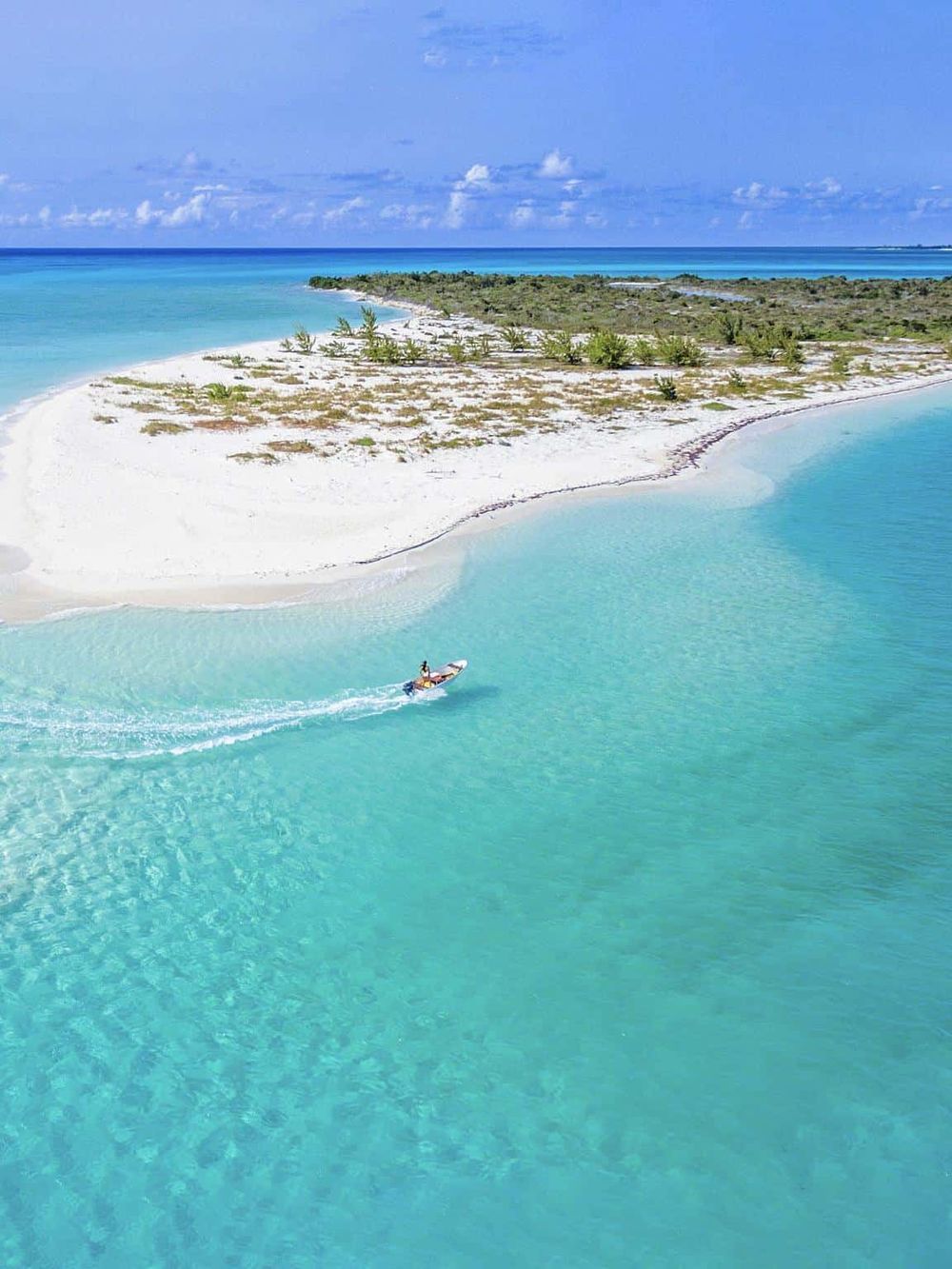 Turquoise waters surrounding a sandy island in a tropical paradise. Idyllic beach with clear blue skies and lush greenery.
