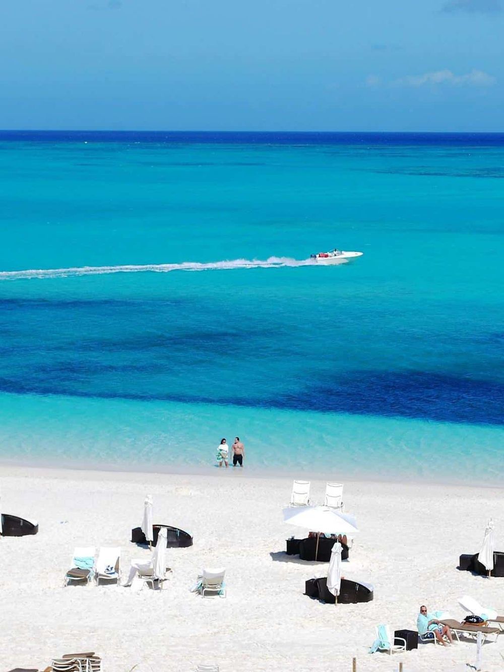 Crystal clear turquoise beach water with boat and people enjoying seaside.