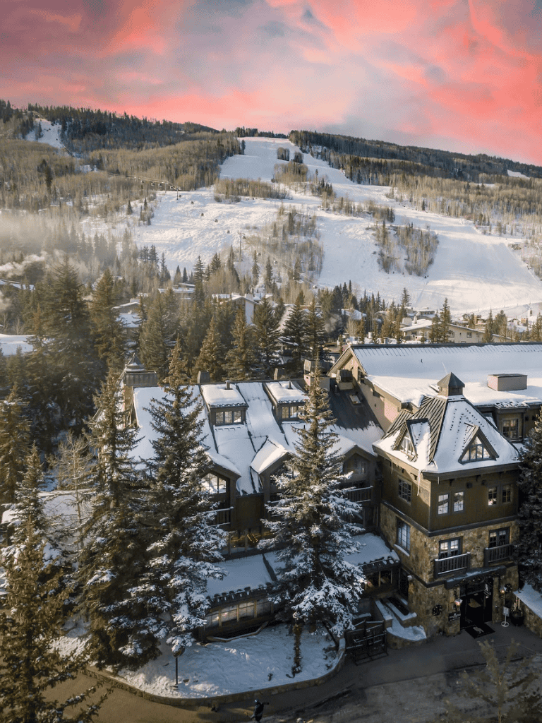 Cozy mountain lodge surrounded by snow-covered trees and slopes at sunset.
