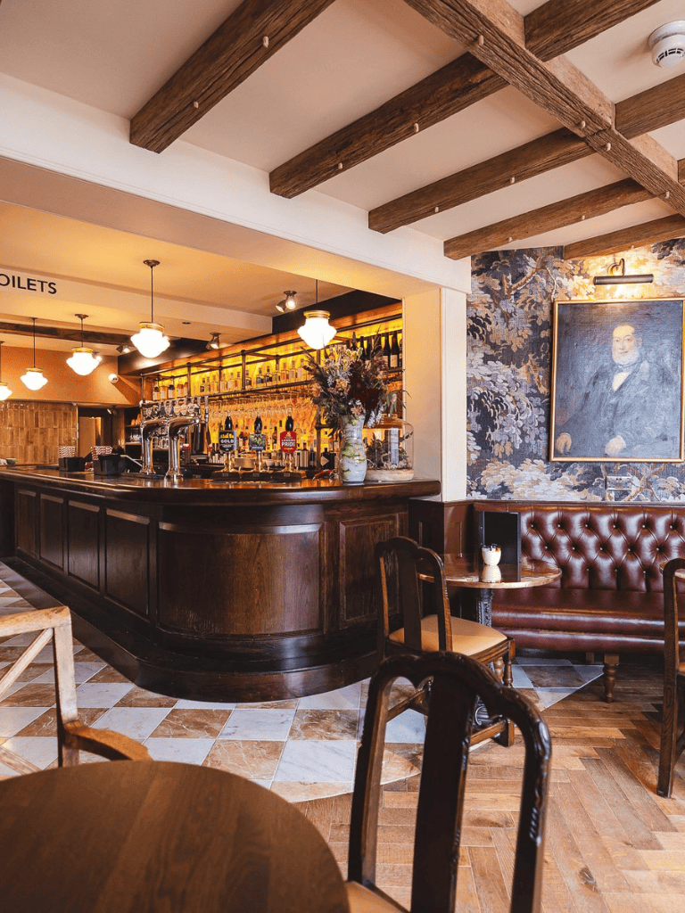 Cozy pub with wooden bar, vintage decor, and floral artwork, perfect for relaxed dining and drinks.